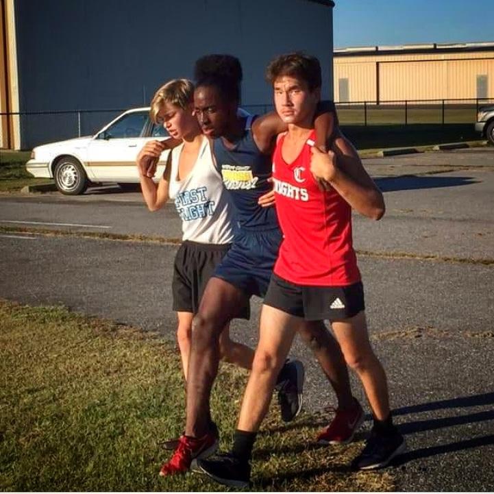 First Flight freshman Jackson Hannon (left) and Currituck’s Andrew Dowdy-Green (right) help Hertford County’s RaQuan Leary (center) cross the finish line at the conference championship on Nov. 9.