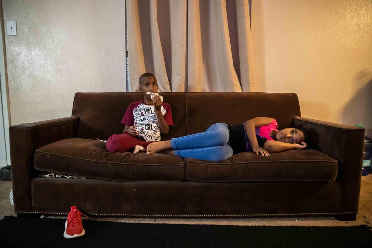 Layal El Dosogi, 7, with her brother Mohammed, 7, watch tv in their living room. The Babiker family’s couch has seen better days. [LOLA GOMEZ / AMERICAN-STATESMAN]